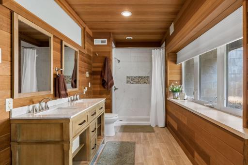 New bathroom recently added with tiled flooring, quartz double vanity top, walk-in tiled shower, redwood walls and ceiling, and a walk-out door to the backyard.