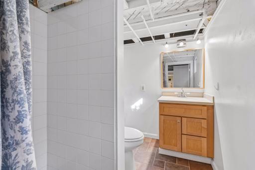 Bright lower-level bathroom with clean tilework, a wood vanity, and a large mirror.
