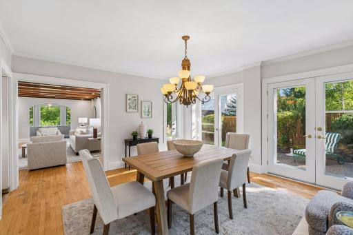 Sunlit dining room with a substantial wood table, elegant chandelier, and garden views.