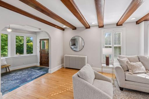 Bright entry area with hardwood flooring, architectural beams, and a classic radiator beneath the windows.