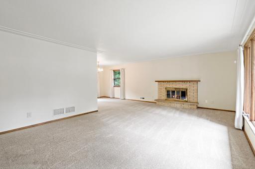Spacious main-level living room featuring new carpet and a cozy fireplace, with an open flow to the dining room and kitchen—ideal for everyday living and entertaining.