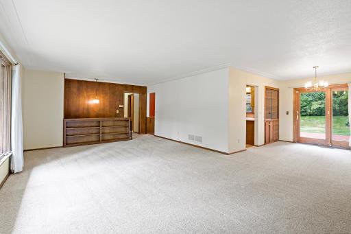 Spacious main-level living room featuring new carpet and a cozy fireplace, with an open flow to the dining room and kitchen—ideal for everyday living and entertaining.