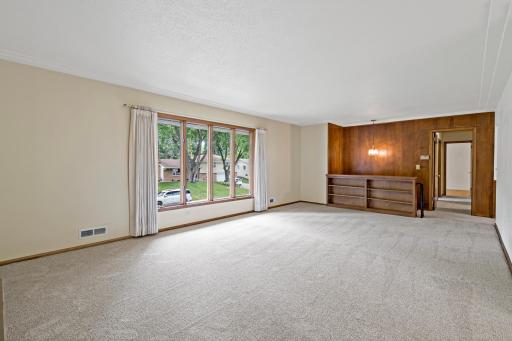 Spacious main-level living room featuring new carpet and a cozy fireplace, with an open flow to the dining room and kitchen—ideal for everyday living and entertaining.