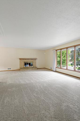 Spacious main-level living room featuring new carpet and a cozy fireplace, with an open flow to the dining room and kitchen—ideal for everyday living and entertaining.