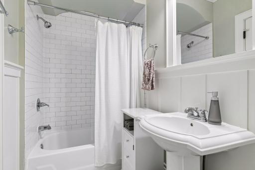The full ceramic tile bath has been remodeled and features a mini hex tile floor, pedestal sink, and subway tile tub/shower surround.