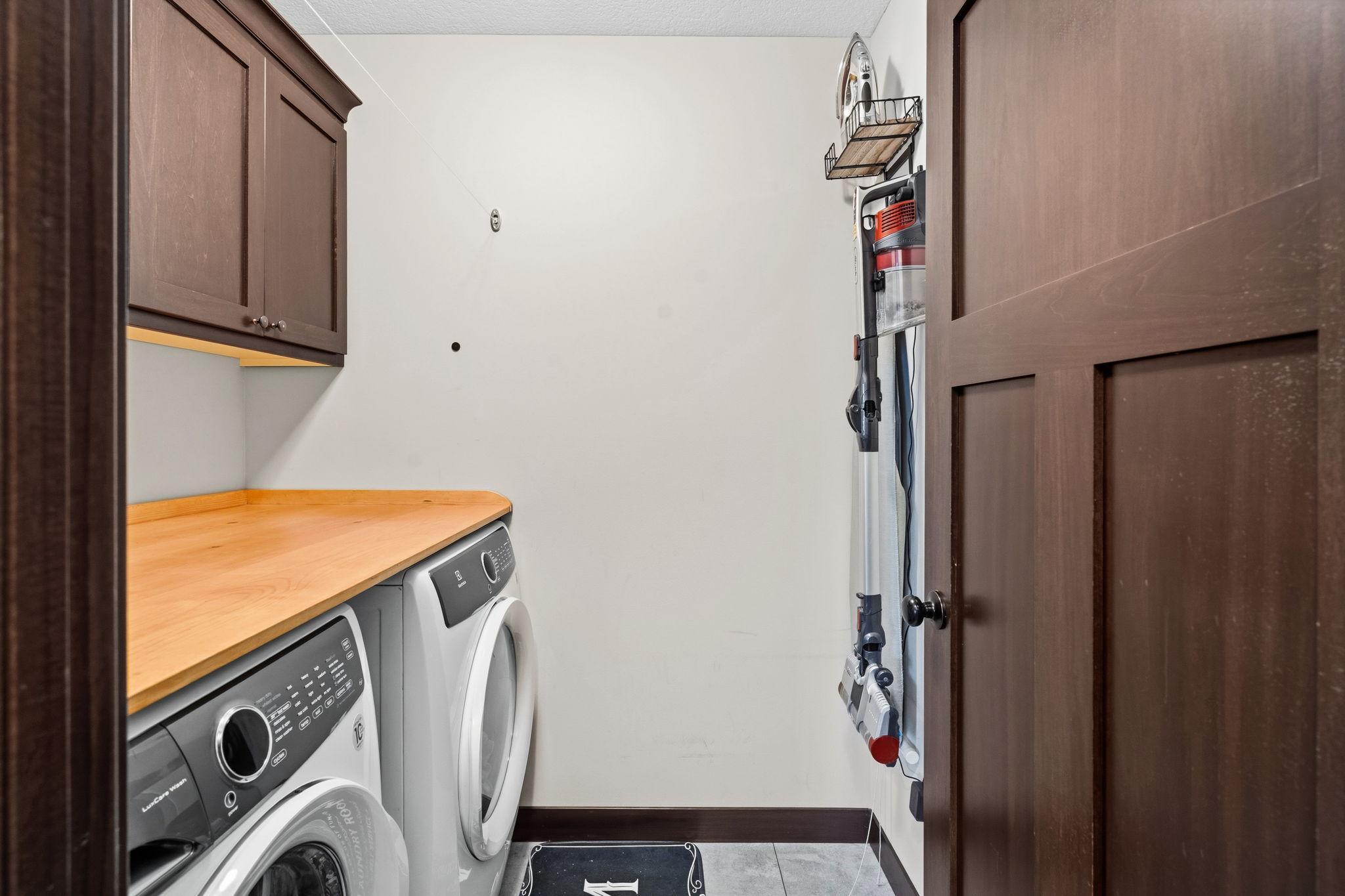 Convenient upper-level laundry room featuring front-loading laundry appliances, built-in cabinetry, and folding counter.