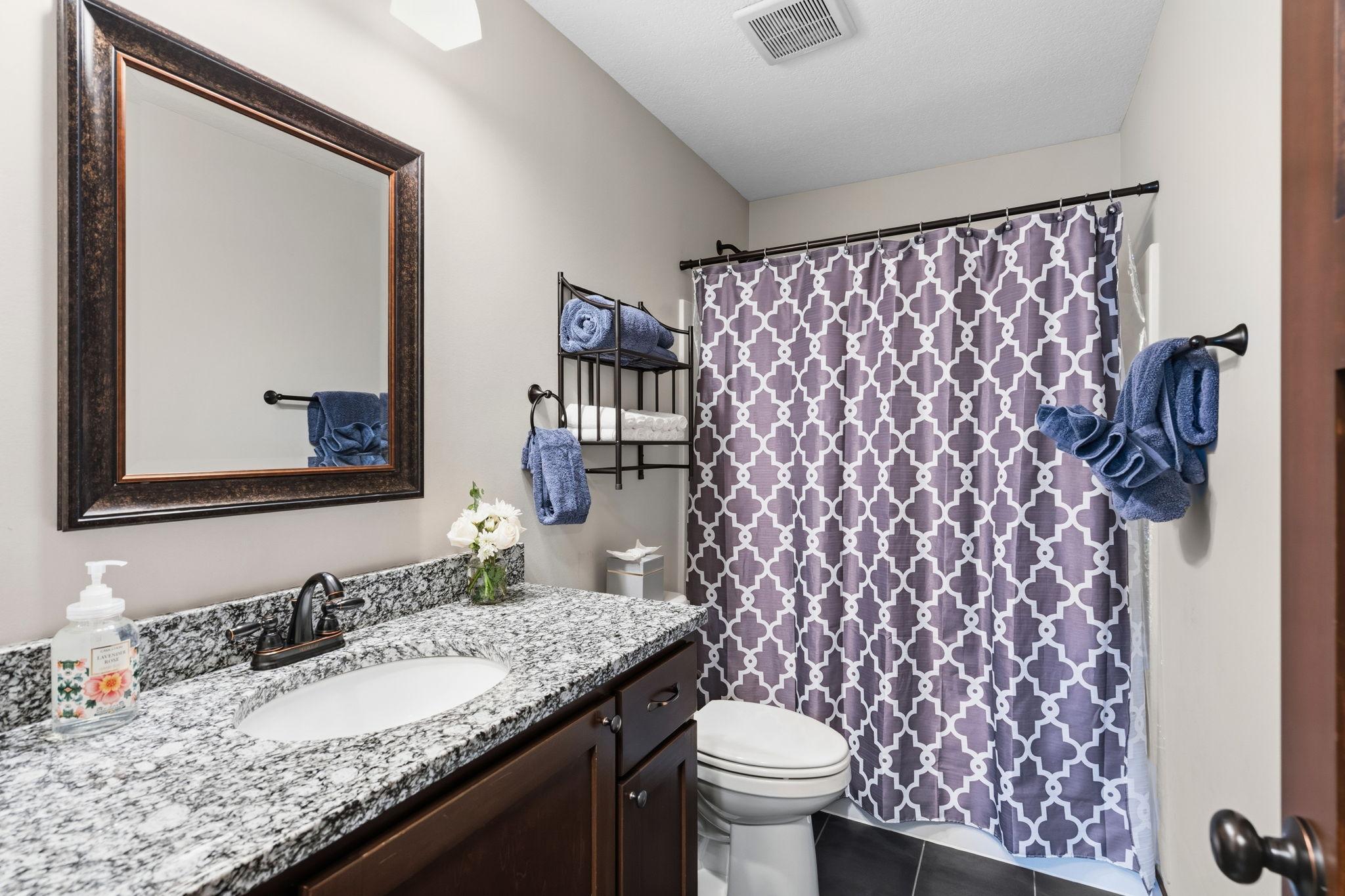 Full bathroom with granite vanity and tub/shower combination.
