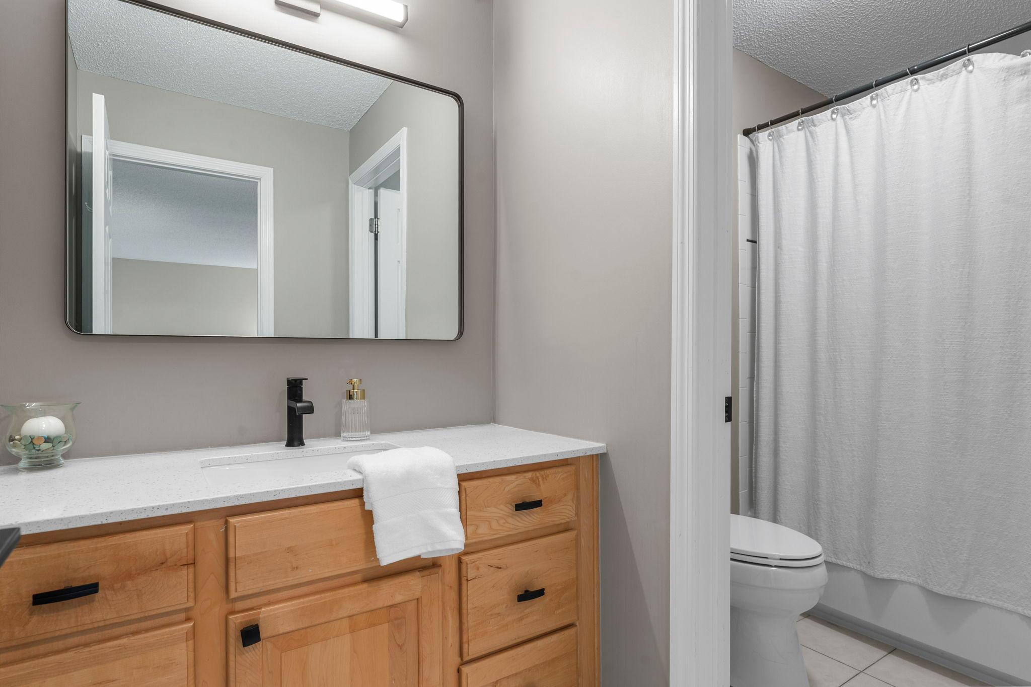 Just steps away is a full bathroom featuring new quartz countertops, updated lighting fixtures, tile flooring, and a separate water closet with a tub and shower combination.