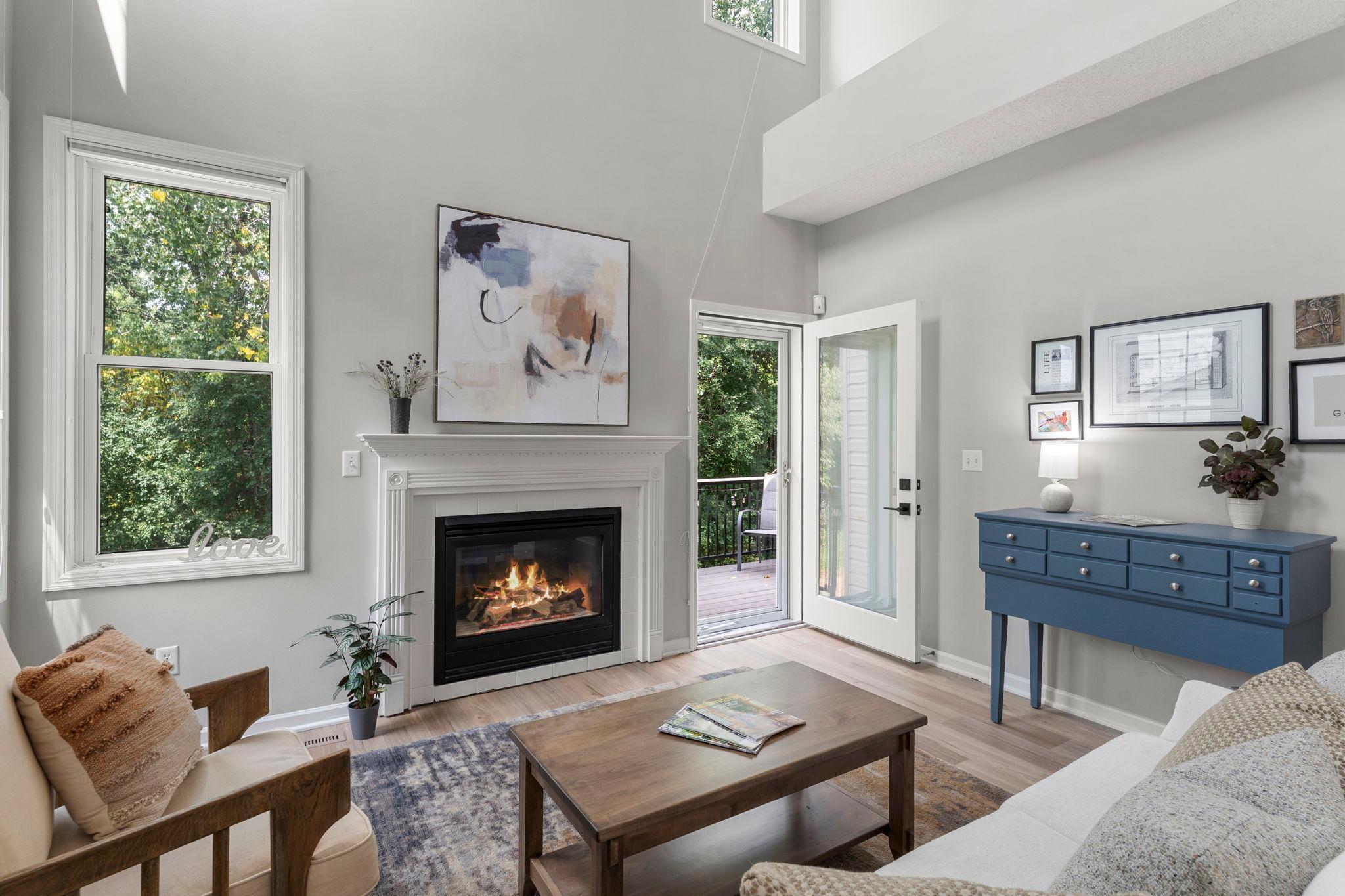 The inviting living room showcases soaring 18-foot ceilings, abundant natural light from numerous windows, a cozy gas fireplace, and access to the 8x10 maintenance-free deck (2024).