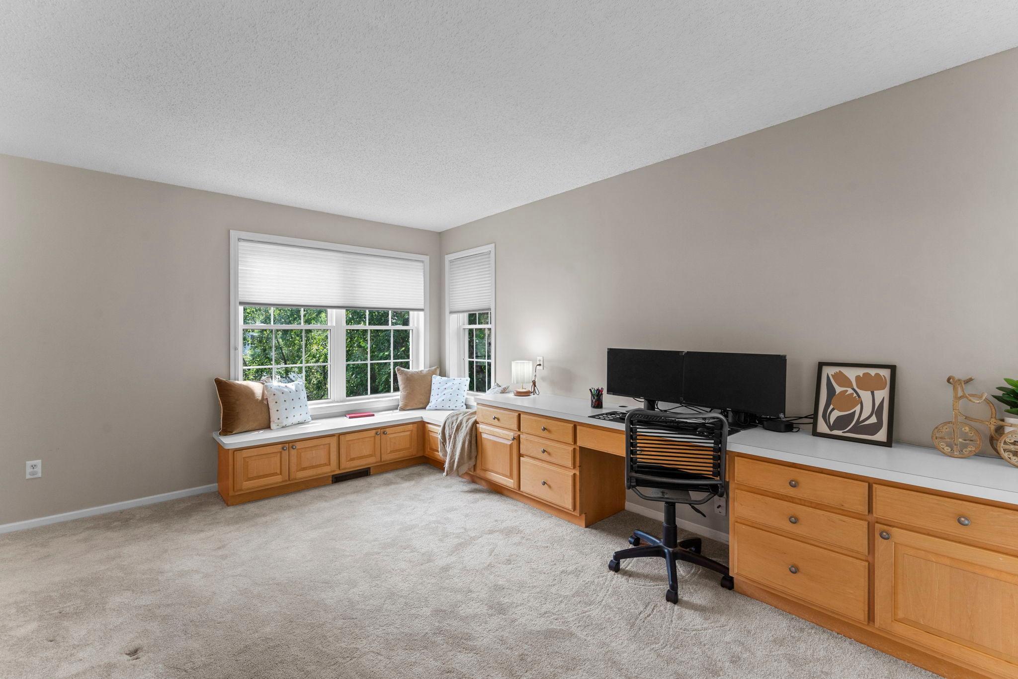 This versatile space features carpeting, built-in desk space, cabinetry, and a bench with windows providing abundant natural light—perfect for a home office, hobby area, or additional living space.
