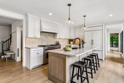 The gourmet eat-in kitchen is beautifully appointed with a center island, quartz countertops, custom enameled and stained cabinetry, and a Wolf gas range.