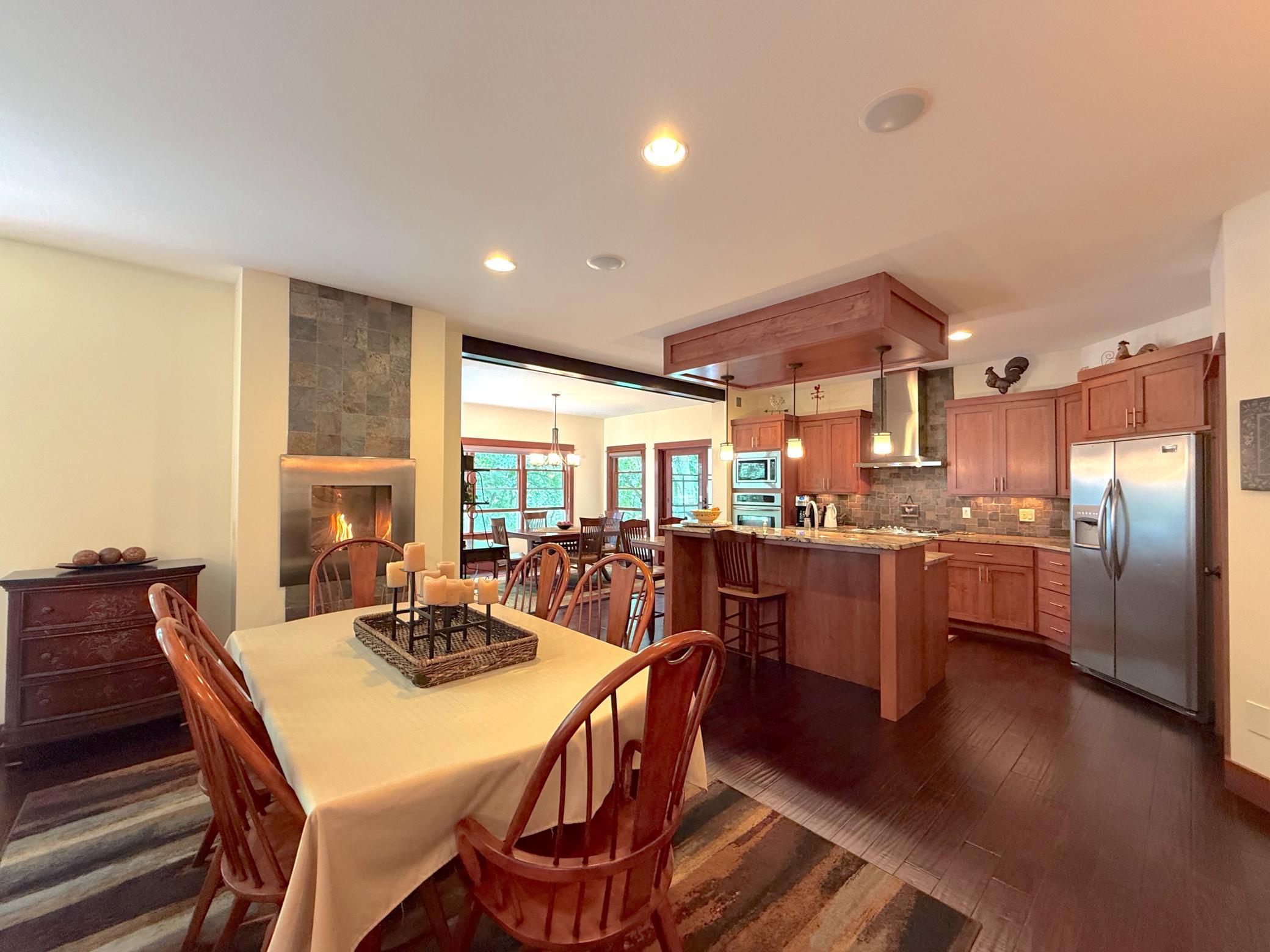 The open-concept kitchen and dining area seamlessly blend warmth and functionality, featuring custom cabinetry, a center island, and a striking fireplace centerpiece.
