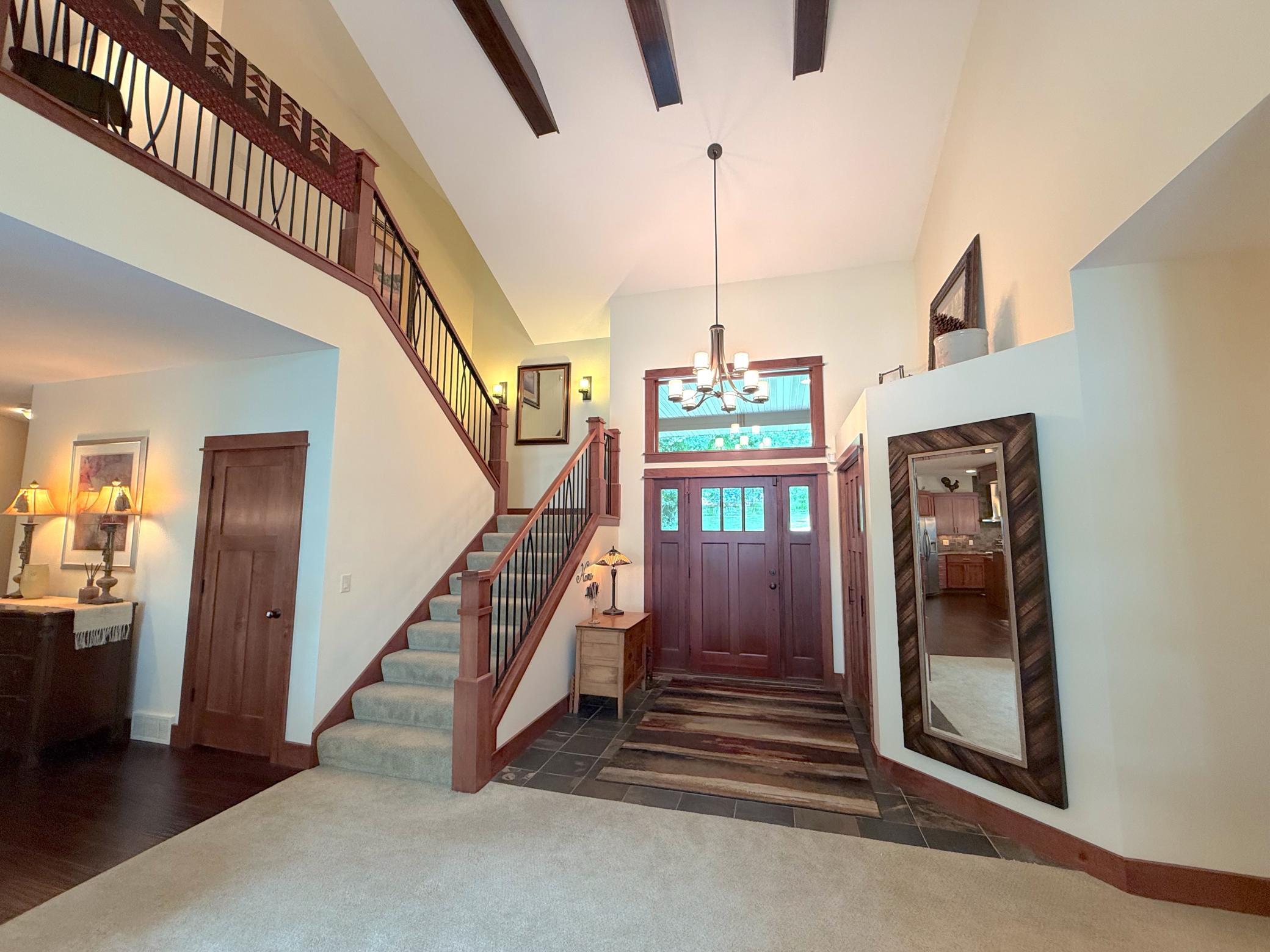 Step into a grand foyer featuring soaring ceilings, exposed wood beams, and an elegant staircase that creates an unforgettable first impression. Warm wood accents and abundant natural light set the tone for the rest of this beautifully designed home.