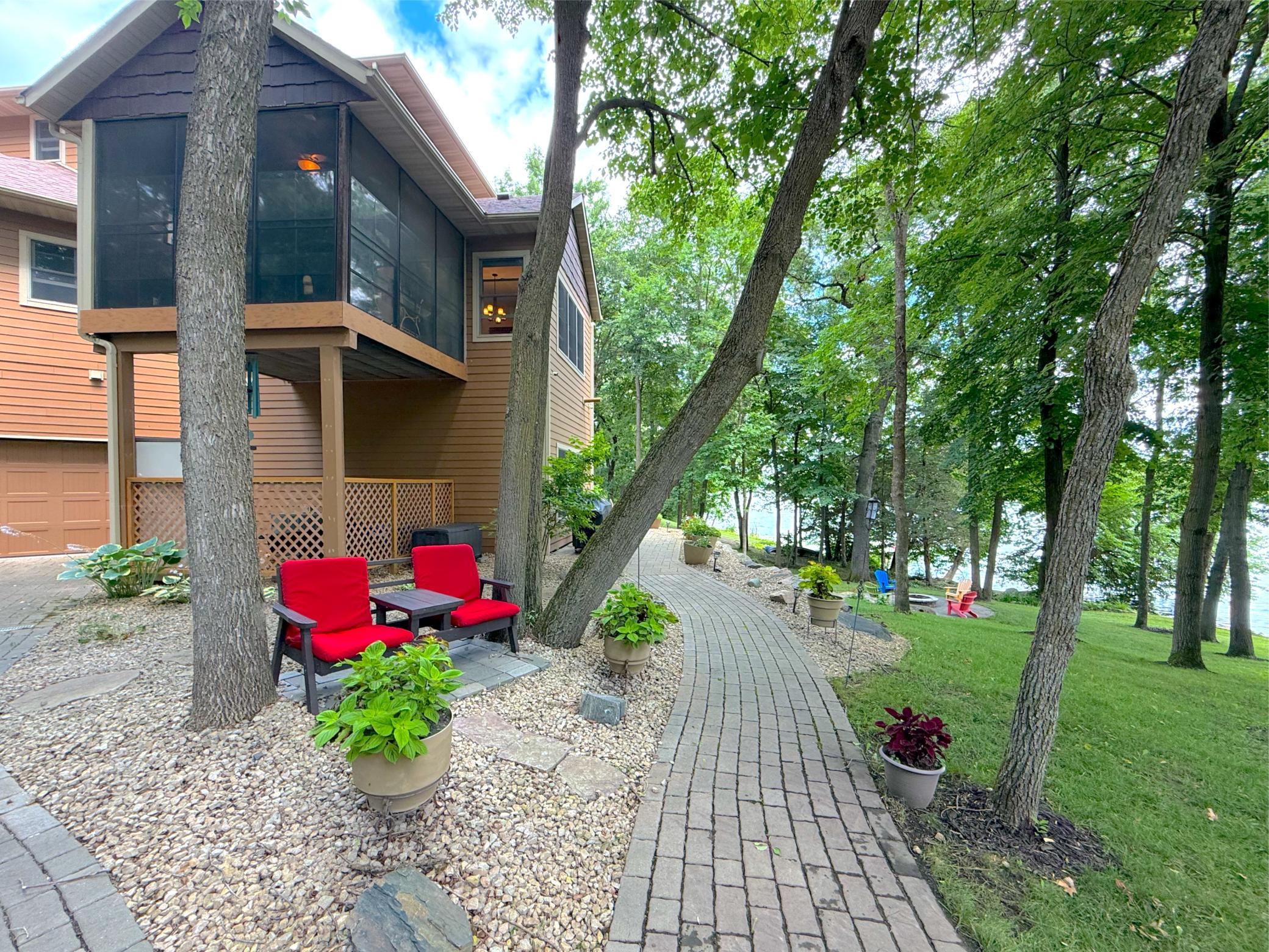 A winding paver pathway leads through the mature trees to the lake, creating a picturesque setting that invites you to explore the property's natural beauty.