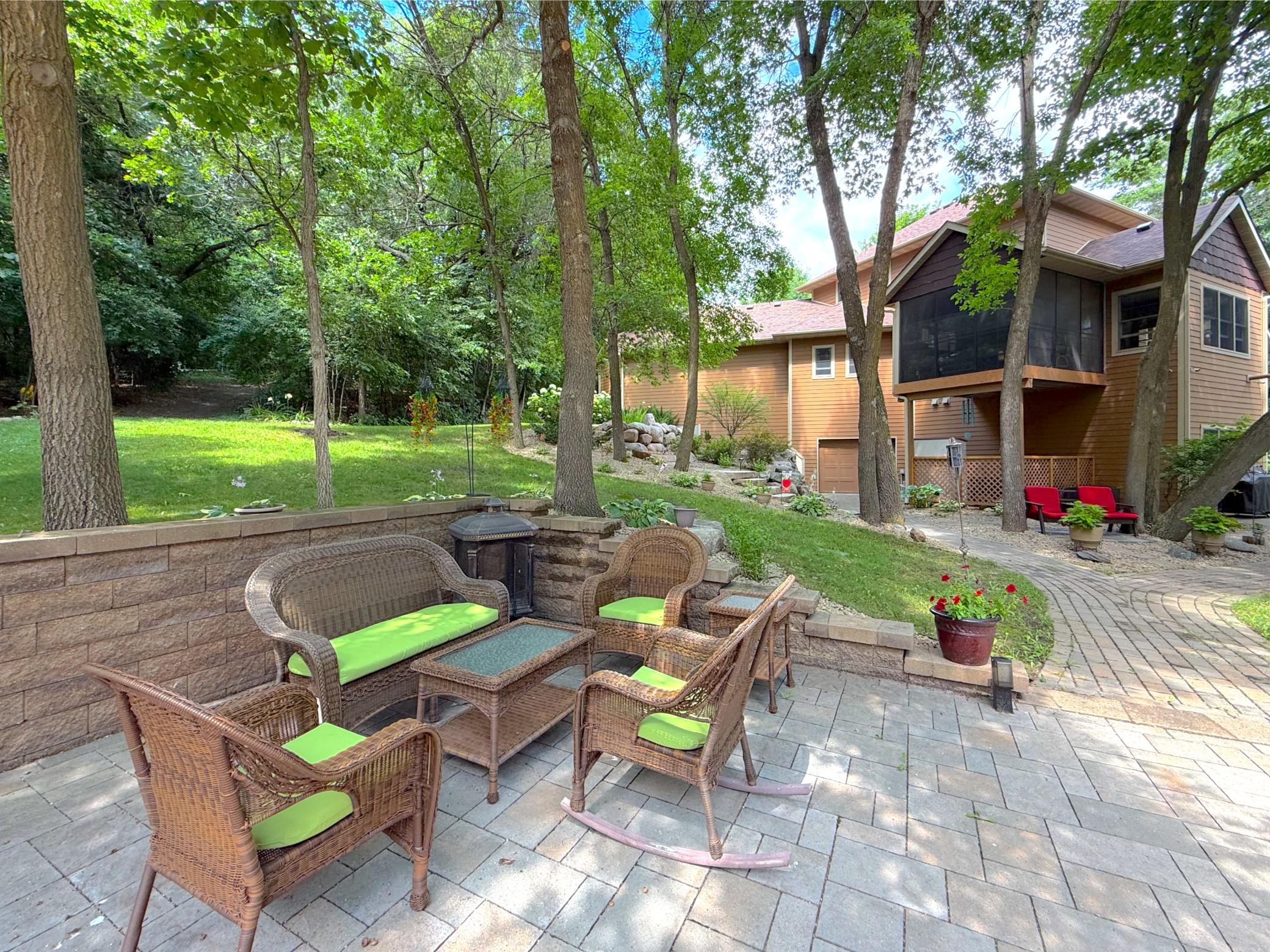 Exceptional outdoor living awaits with a spacious paver patio surrounded by mature trees, lush landscaping, and multiple inviting spaces to gather, relax, and enjoy the peaceful setting.