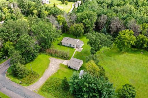 Aerial view of the home with a detached outbuilding/garage, long driveway, and wooded backdrop for privacy.