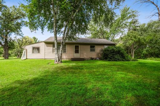 Full view of the homeâs back with sunroom addition and vinyl siding, surrounded by beautiful landscaping.