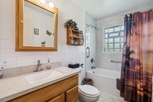 Updated full bath featuring a solid-surface vanity, tile accents, and a tub/shower combination with a glass block window for natural light.