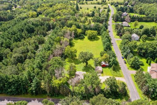 Stunning aerial view highlighting the acreage, open grassy expanse, mature trees, and detached red outbuilding for storage or hobby use.