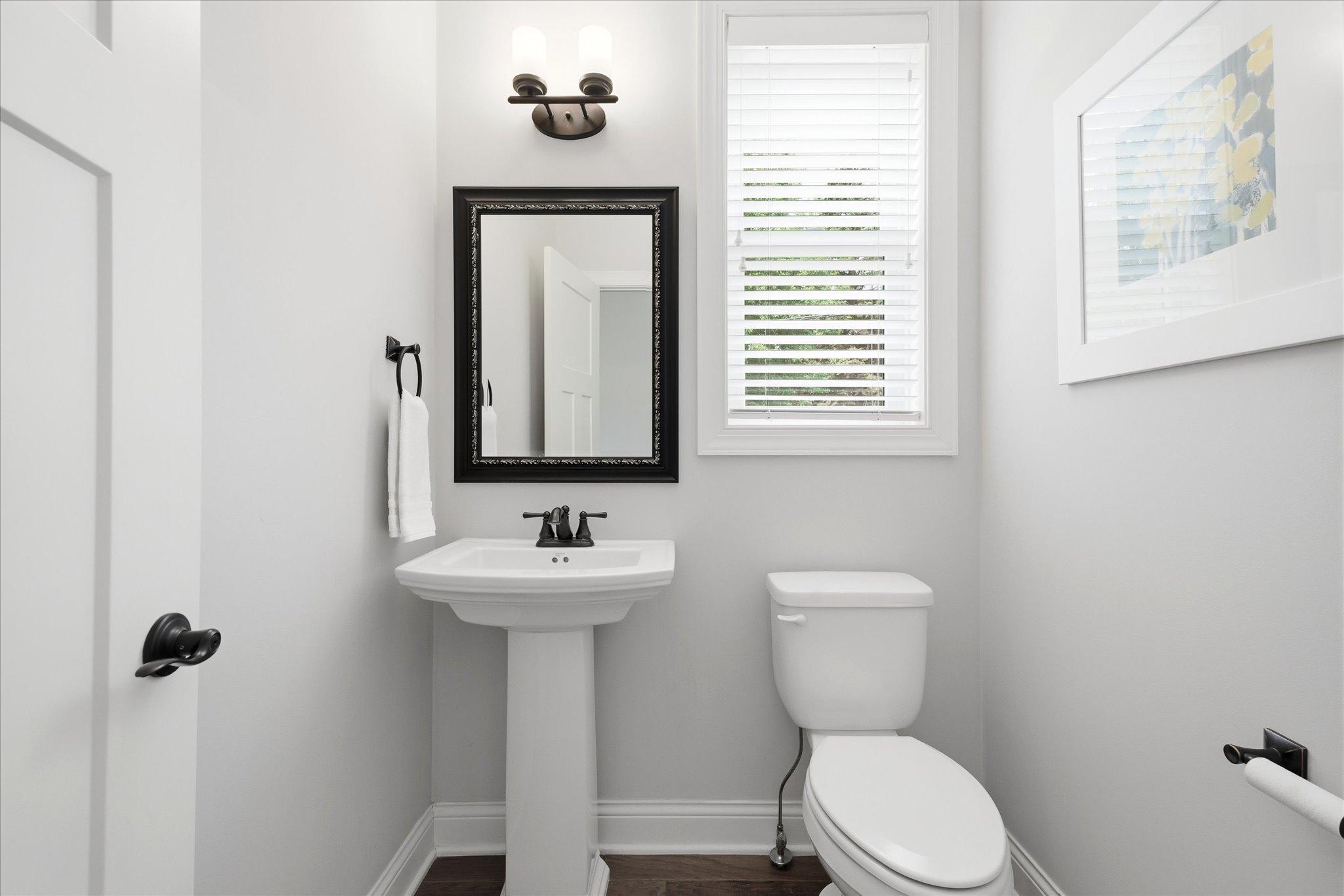 Convenient main-level half bath features a pedestal sink, updated lighting, and a bright window for added natural light.