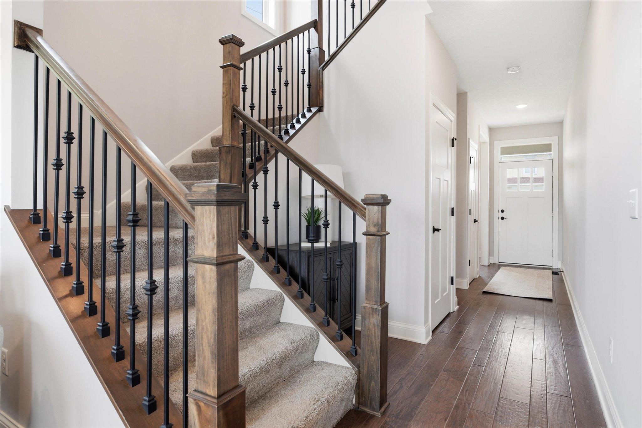 Open staircase with rich wood railings and wrought iron balusters creates an elegant focal point, while the spacious entry hallway showcases beautiful hardwood flooring and a thoughtfully designed layout.