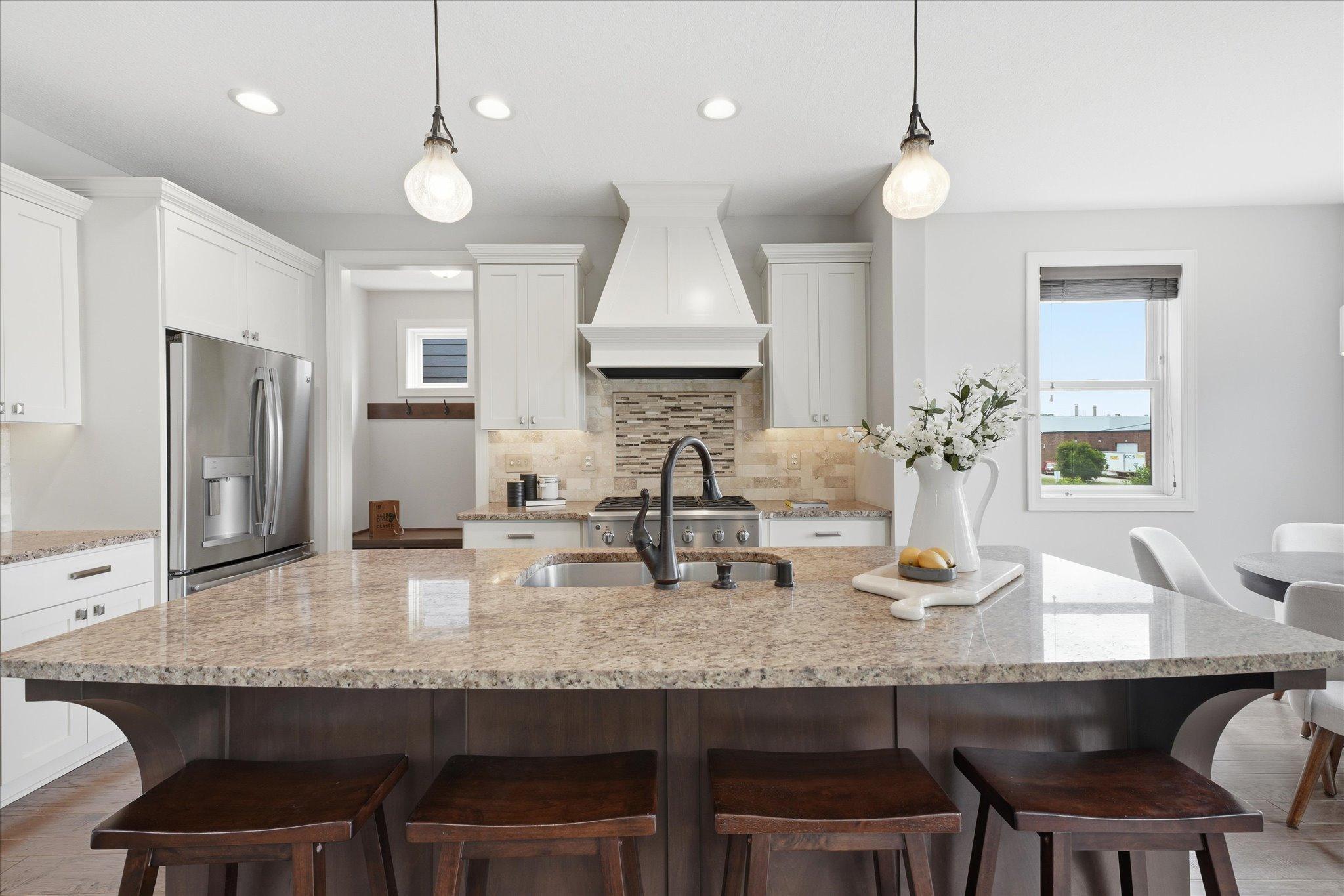 Stunning kitchen is highlighted by an oversized granite island, custom range hood, tile backsplash, abundant cabinetry, and ample prep space for cooking and entertaining.