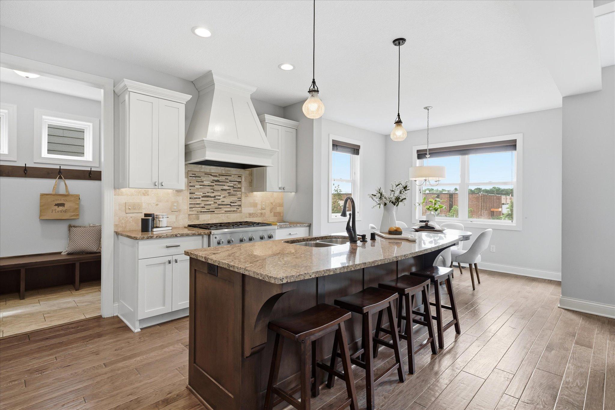 Chef-inspired kitchen features a large center island with seating, granite countertops, custom cabinetry, stainless steel appliances, designer lighting, and an adjacent informal dining area.