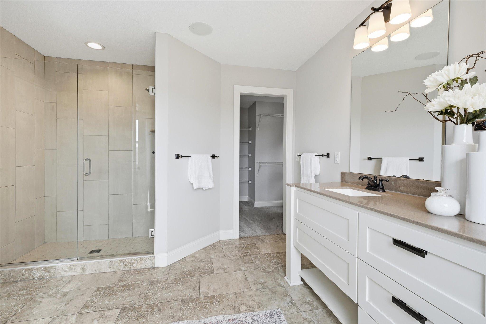 Oversized walk-in tile shower features frameless glass doors, and elegant tile surround.