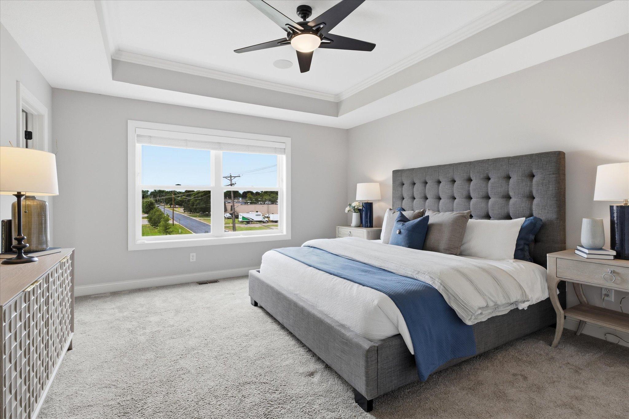 Luxurious primary suite features a tray ceiling with crown molding, plush carpeting, oversized windows, surround sound, and generous space for a king-size bedroom set.