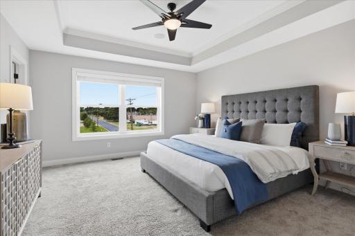 Luxurious primary suite features a tray ceiling with crown molding, plush carpeting, oversized windows, surround sound, and generous space for a king-size bedroom set.