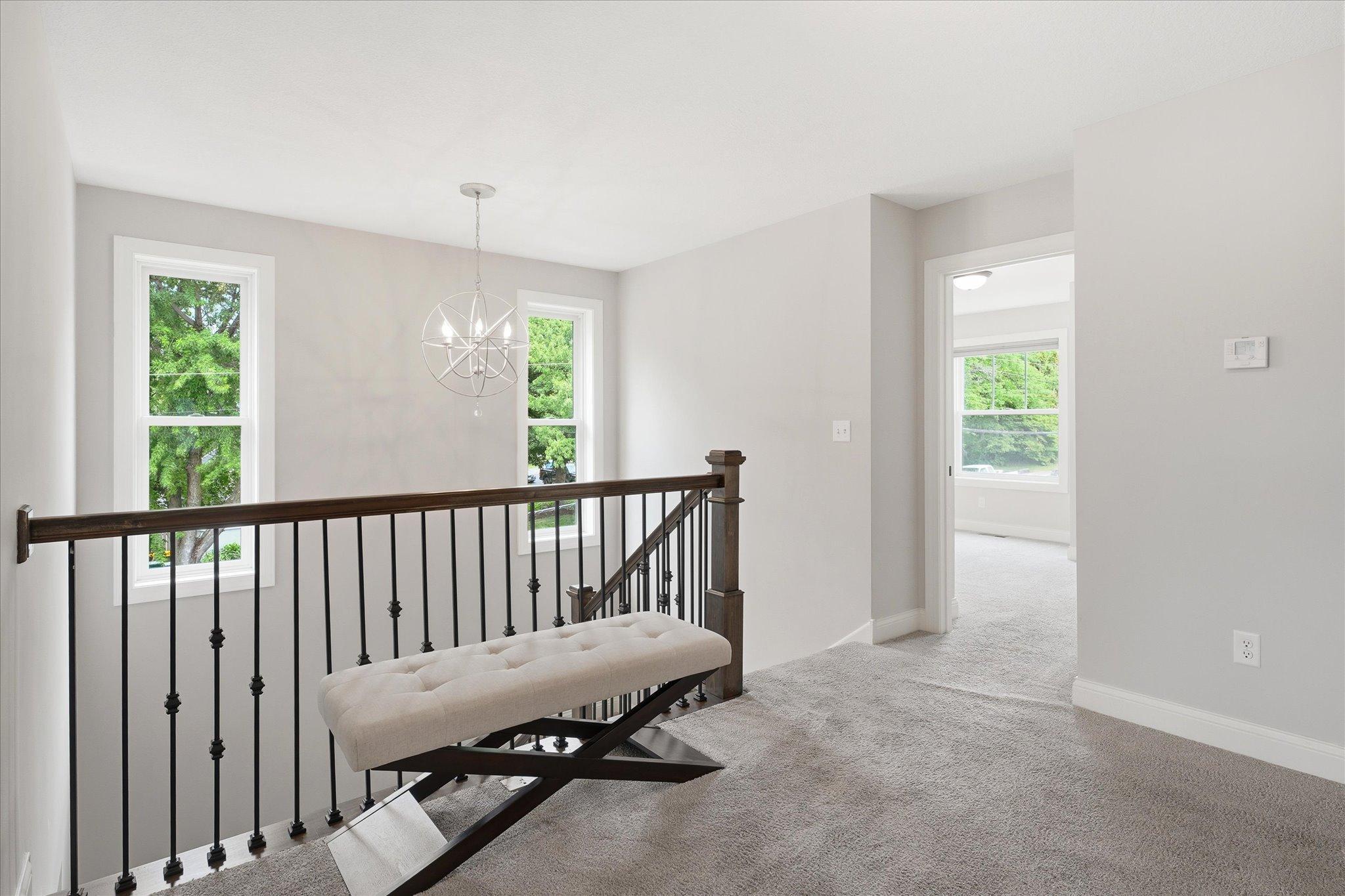 Open upper-level landing creates an inviting transition between all four bedrooms, featuring abundant natural light, elegant staircase railing, and a stylish statement chandelier.