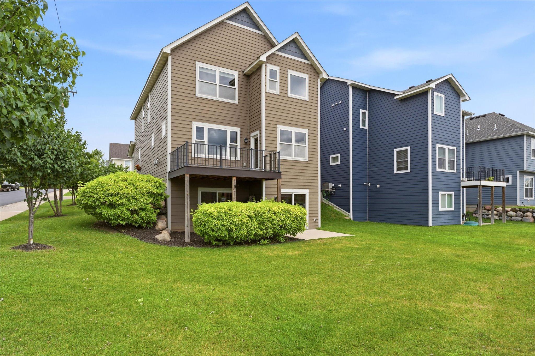 Beautiful rear elevation showcases the home's attractive curb appeal, maintenance-free exterior, spacious deck, walkout lower level, and professionally landscaped yard.