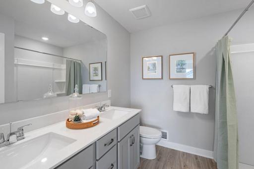 A peak inside the bathroom off the Primary Suite. Notice the extra high cabinets and double-bowl Quartz covered vanity with loads of storage! Photo is of actual home. Colors and options may vary. Ask Sales Agent for details.