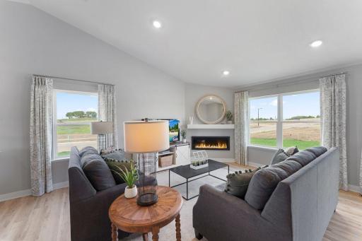 The living room is punctuated by an electric fireplace-which serves as a cozy bookend to the area and highlights a space that's flooded in natural light via soaring windows overlooking the back of the home! Photo is of actual home.