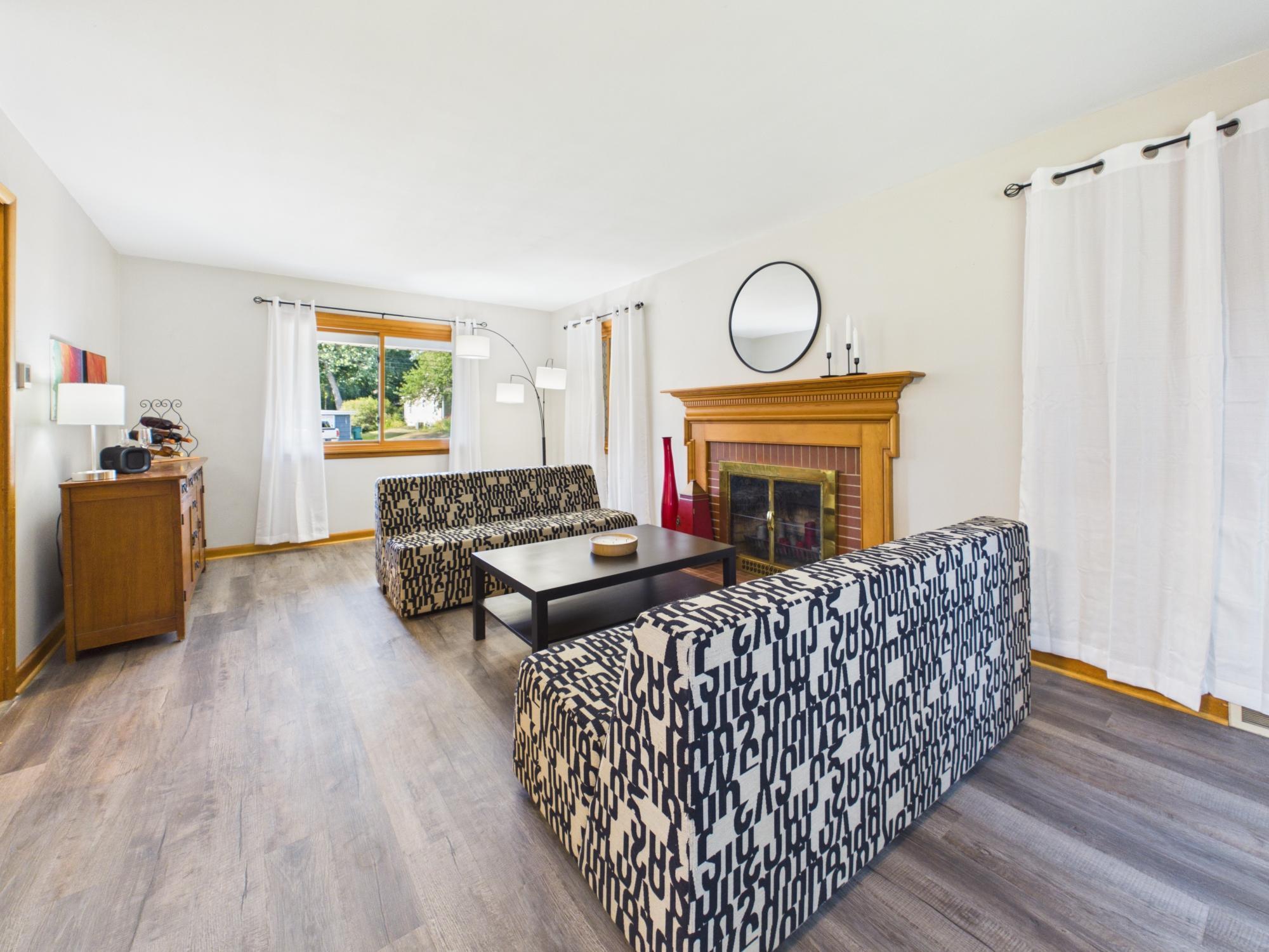 Living room looking toward the fireplace, showcasing the updated flooring, neutral finishes and bright, comfortable gathering space.