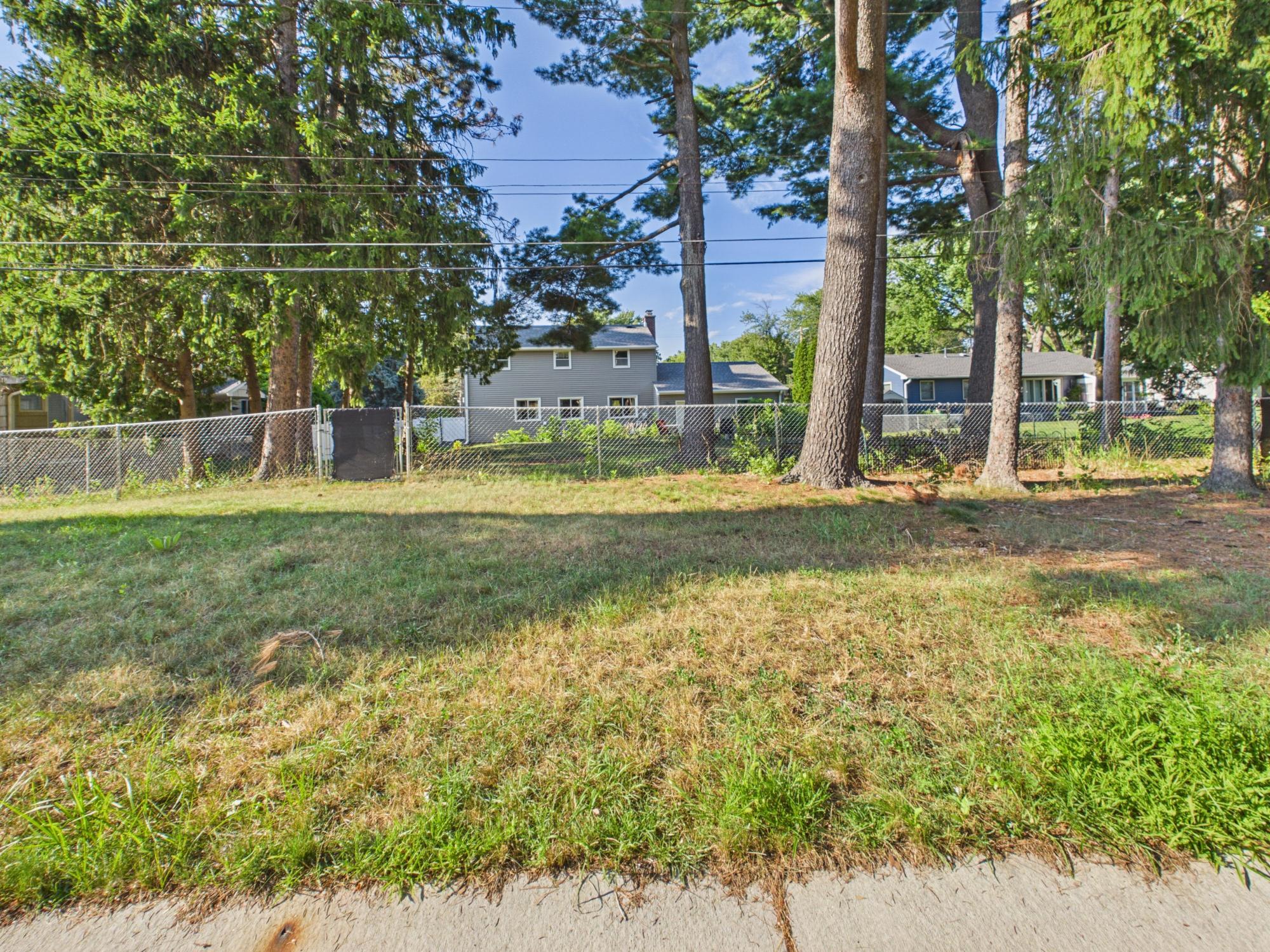 Additional view along the fenced backyard showing the mature tree canopy and open lawn.