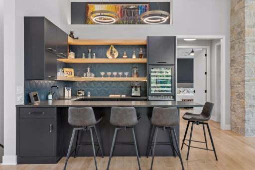 Stylish wet bar with room for seating, sink, beverage fridge, and stylish backsplash and lighting