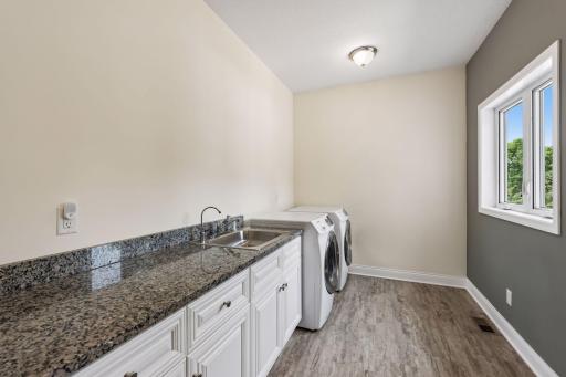 Convenient upper level laundry room with granite countertops, utility sink, abundant cabinetry, and plenty of workspace to keep everyday tasks organized.