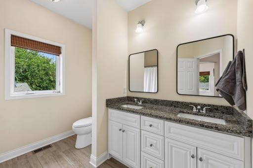A spacious dual-sink vanity with granite countertops provides convenience for busy mornings, while the thoughtful layout offers privacy between the vanity and bath area.