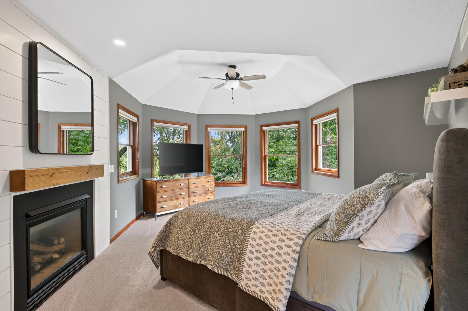 The luxurious primary suite is a true retreat with a gas fireplace, ceiling fan, tray ceilings, oversized windows overlooking nature and mature trees, and even a hidden safe