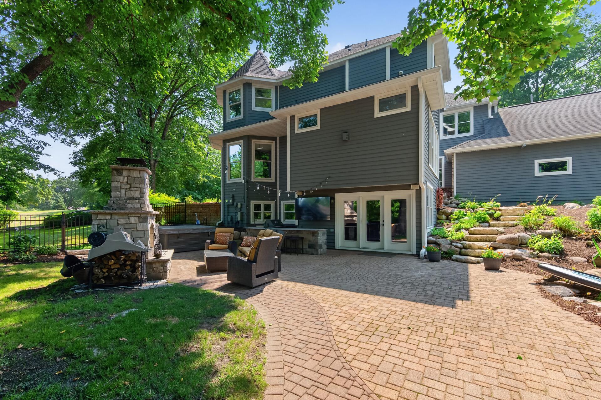 Enjoy your privacy in this unique, fully enclosed backyard with lush perennial gardens, expansive patios, an outdoor fireplace, a fully equipped outdoor kitchen, TV, and a private hot tub retreat.