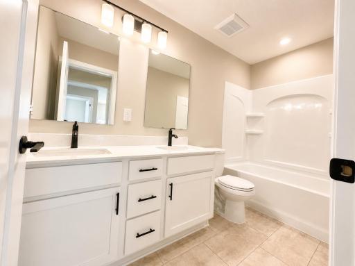 (Photo is of the actual home.) This shared full bathroom features dual sinks and a shower-tub combination.