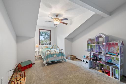 Next to the primary bedroom is a cozy, carpeted room featuring a ceiling fan and large window positioned above the bed.