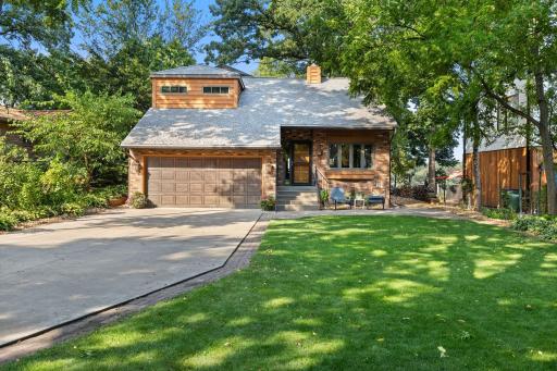 Inviting front exterior featuring a classic brick facade, attached double garage, front patio sitting area and lush lawn.