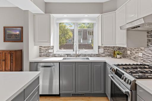 Light pours in through the window over the sink, illuminating crisp white and gray cabinetry and gleaming quartz countertops.