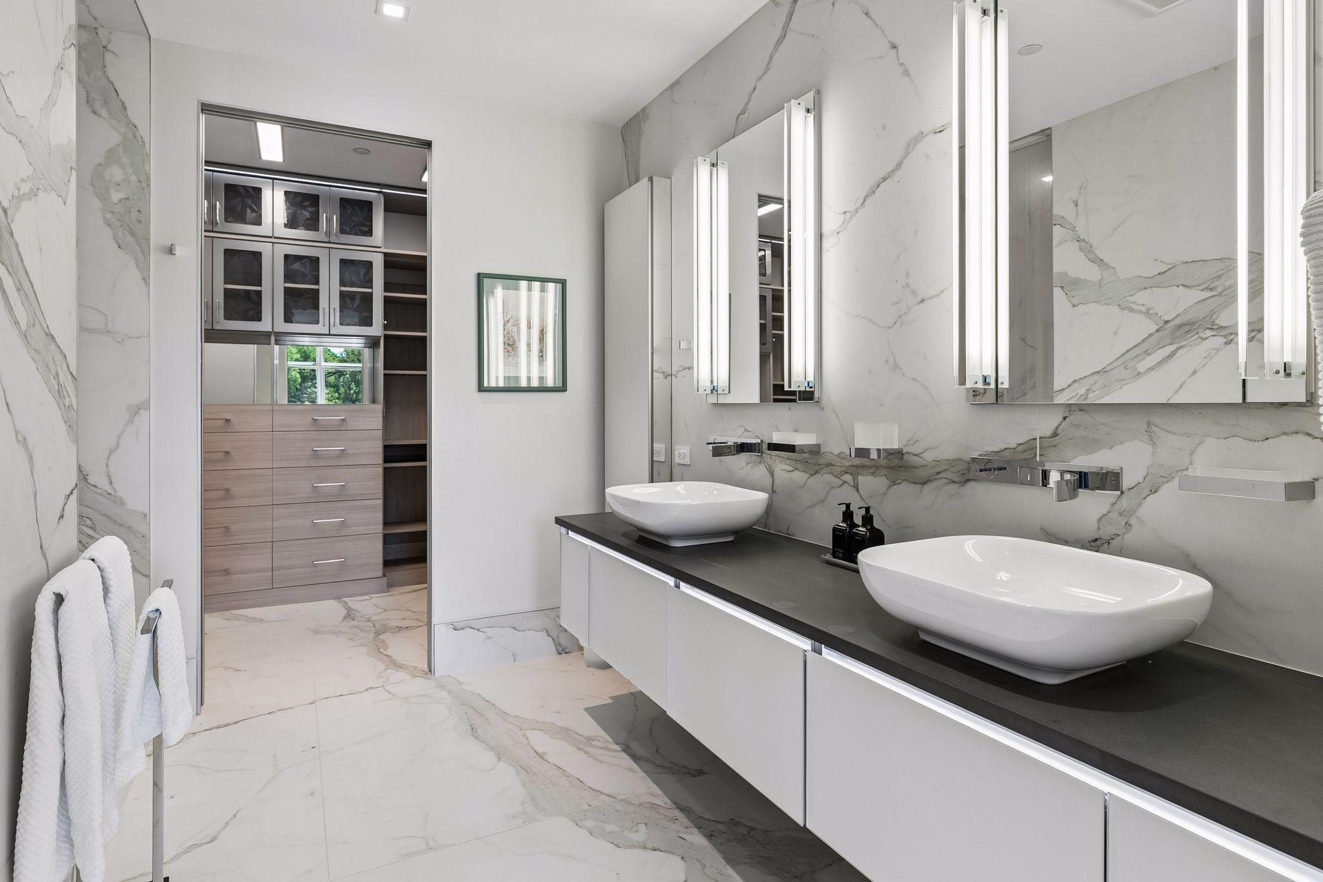 Primary bathroom features double sinks, porcelain flooring and walls, walk in shower, and walk-in closet