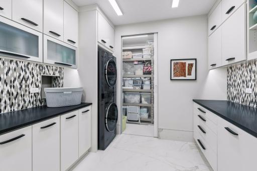 Features extensive built-in storage, sleek countertops, and a convenient pocket door connecting directly to the primary walk-in closet for effortless laundry drop-off.