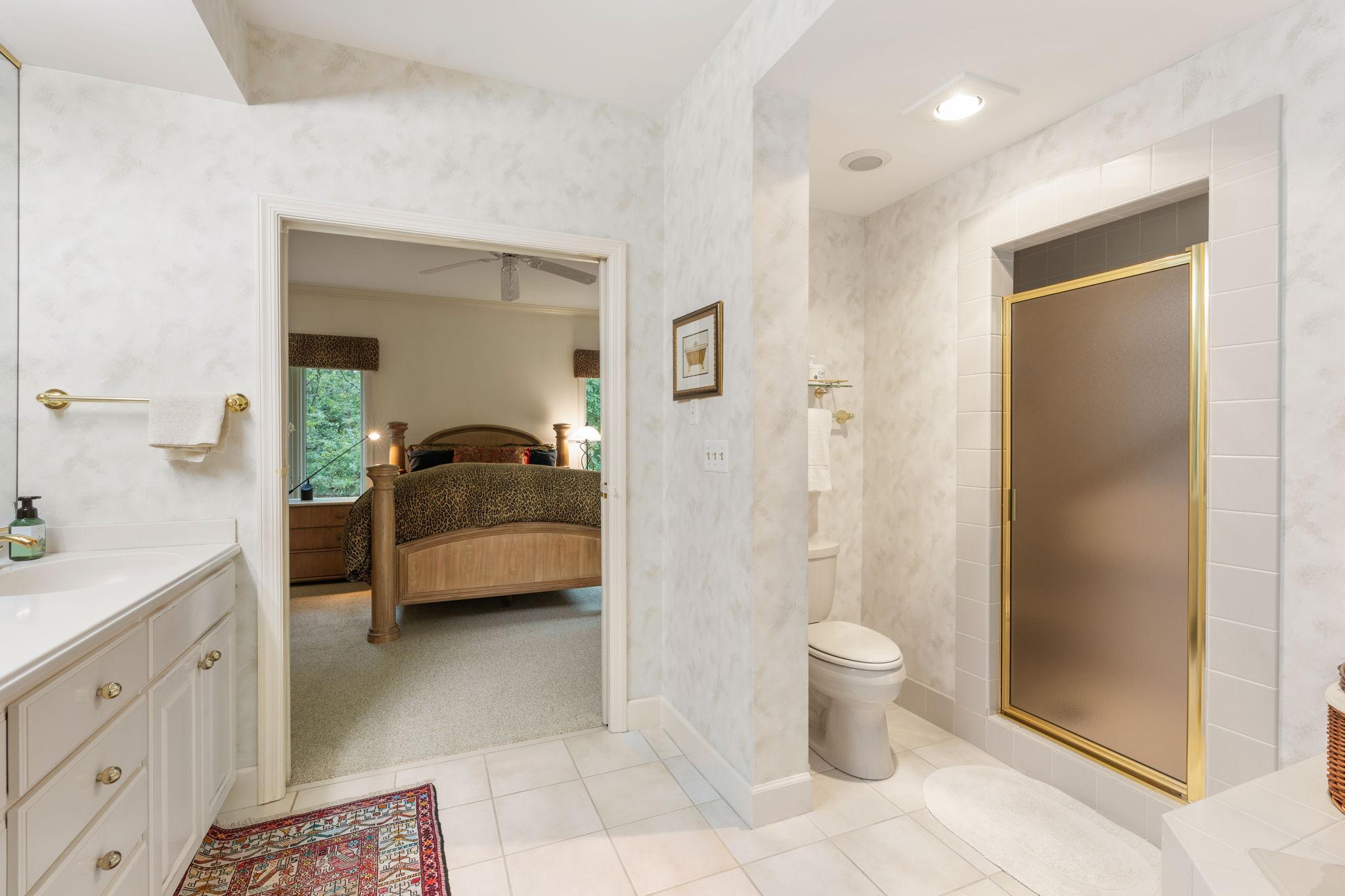 This bathroom features a double vanity sink, walk in shower with grab bars, and a luxurious soaking tub.