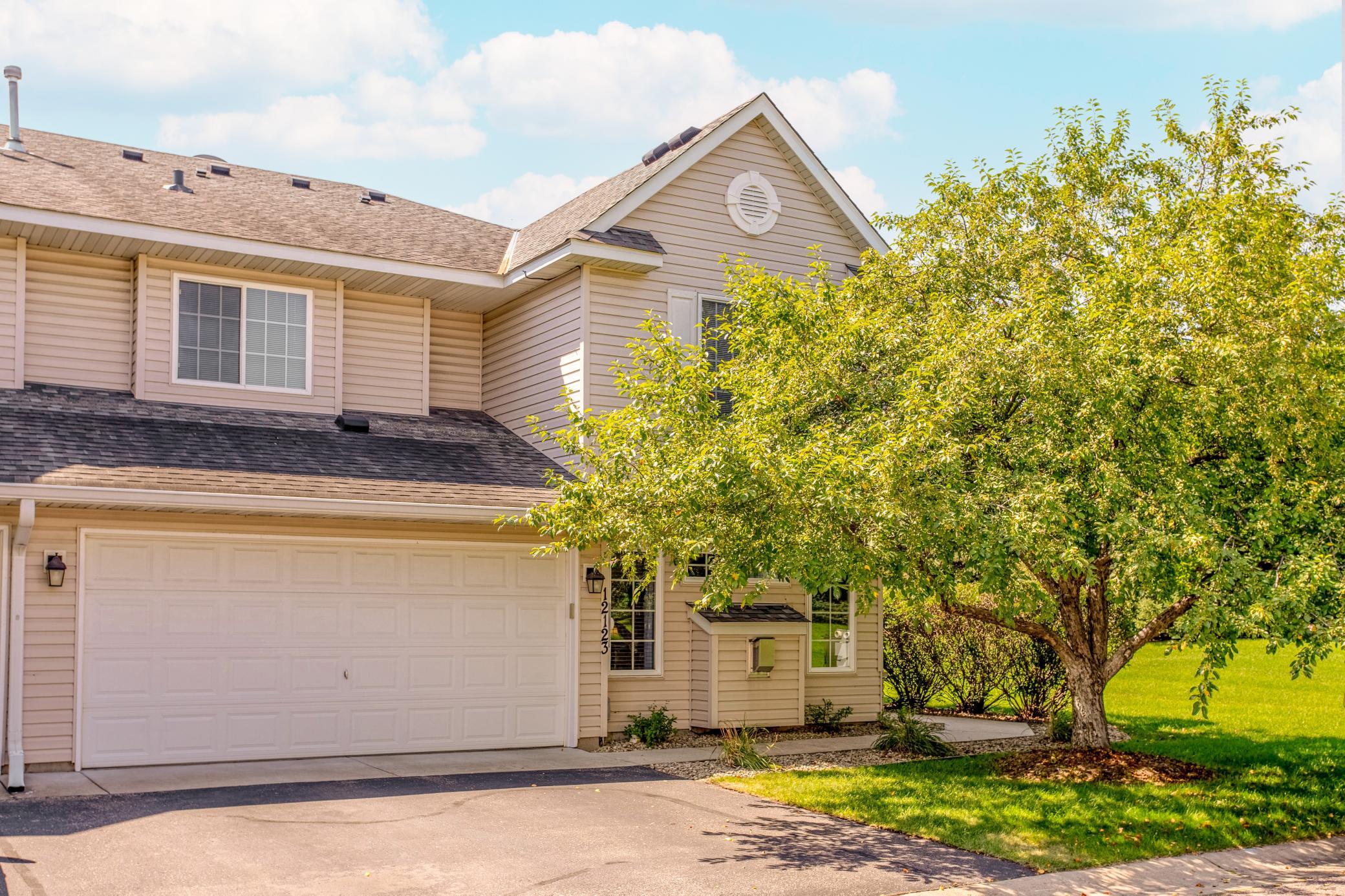 Attractive side-by-side townhome with an attached two-car garage, mature shade tree, and inviting private entrance.