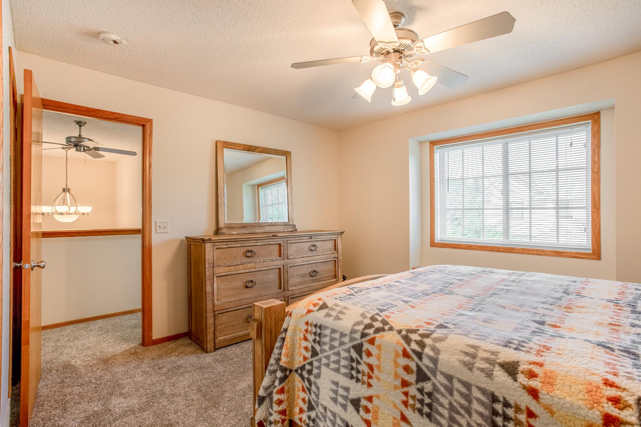 Bright primary retreat with a large window, warm wood trim, ceiling fan, and brand-new carpeting.